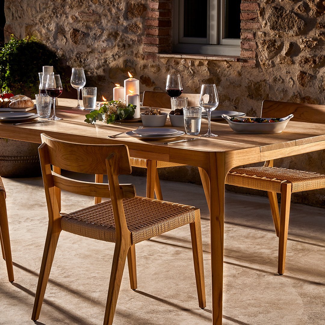 "Warm wooden dining table with natural grain, complemented by neutral-toned woven chairs in an outdoor setting."