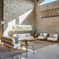 Modern beige and white sofa set with natural wood detailing, complemented by a light gray rug and stone walls.