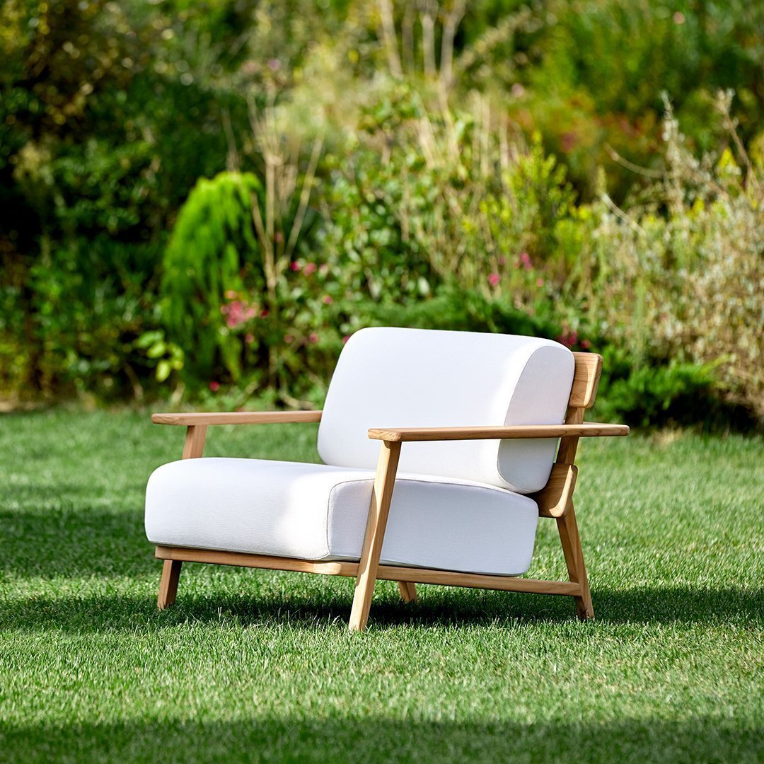 White outdoor sofa with natural wood frame, set against a lush green garden backdrop. Simple and modern design.