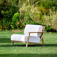 White outdoor sofa with natural wood frame, set against a lush green garden backdrop. Simple and modern design.