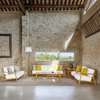 Bright yellow and white cushions adorn natural wood furniture in a rustic stone interior with warm earthy tones.