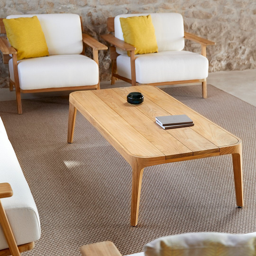Natural oak coffee table with smooth lines, paired with white chairs and bright yellow cushions on a textured beige rug.
