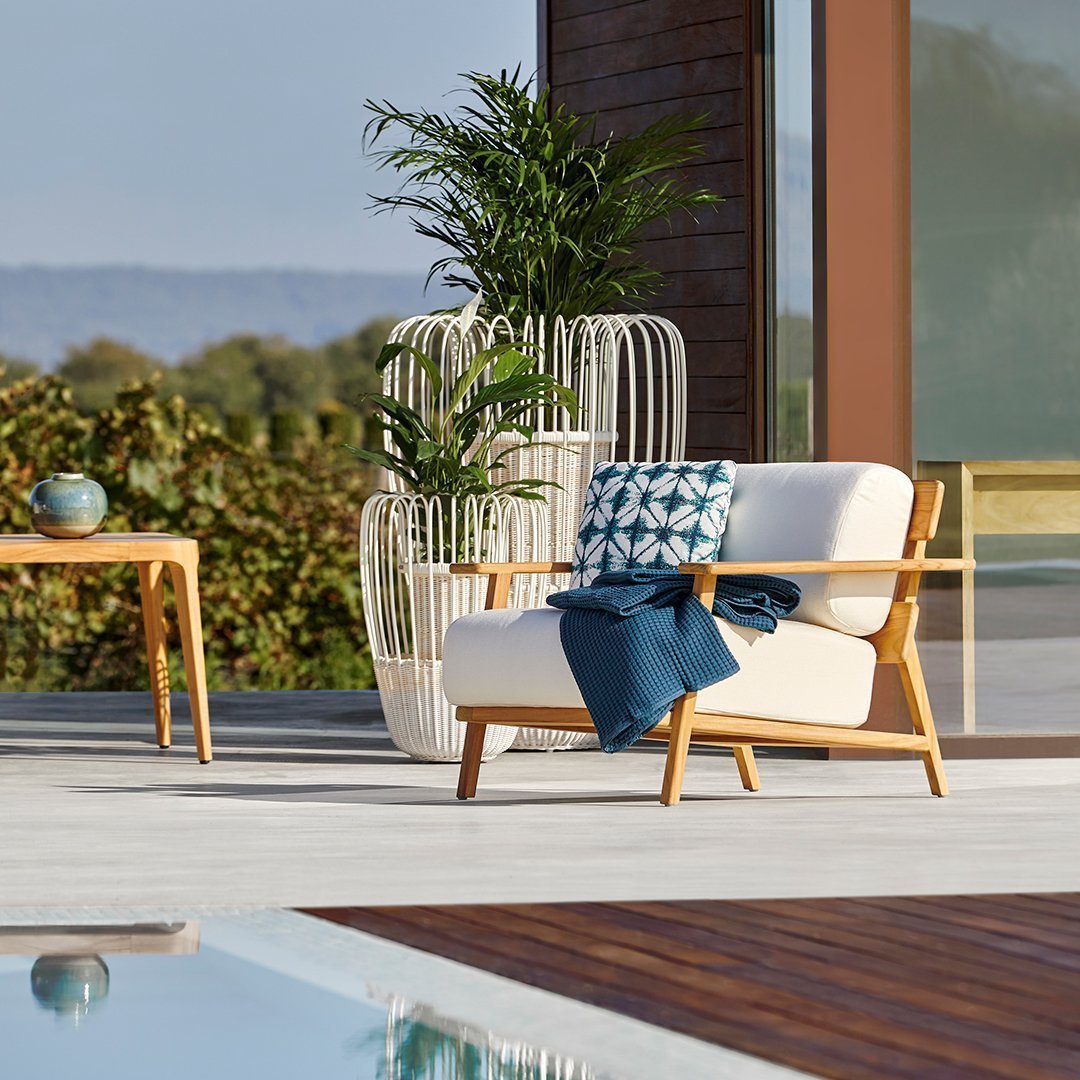 Cozy outdoor chair in cream with teal and navy patterned cushion, paired with natural wood accents and vibrant greenery.