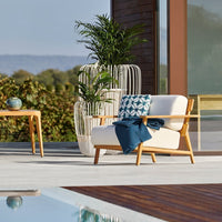 Cozy outdoor chair in cream with teal and navy patterned cushion, paired with natural wood accents and vibrant greenery.