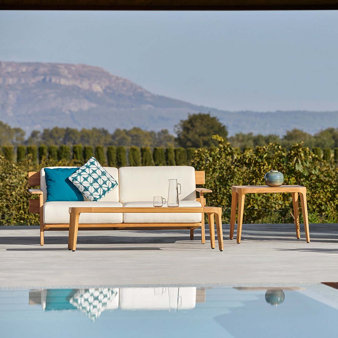Elegant outdoor lounge set featuring a white sofa, a blue and white patterned cushion, and natural wooden accents.