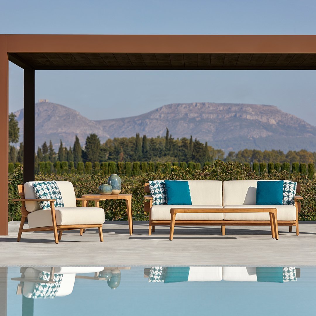 "Elegant outdoor furniture with neutral cushions and vibrant blue geometric patterns, set against a serene mountain backdrop."