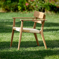 Light wood chair with natural finish and woven beige seat, surrounded by green grass and soft outdoor lighting.
