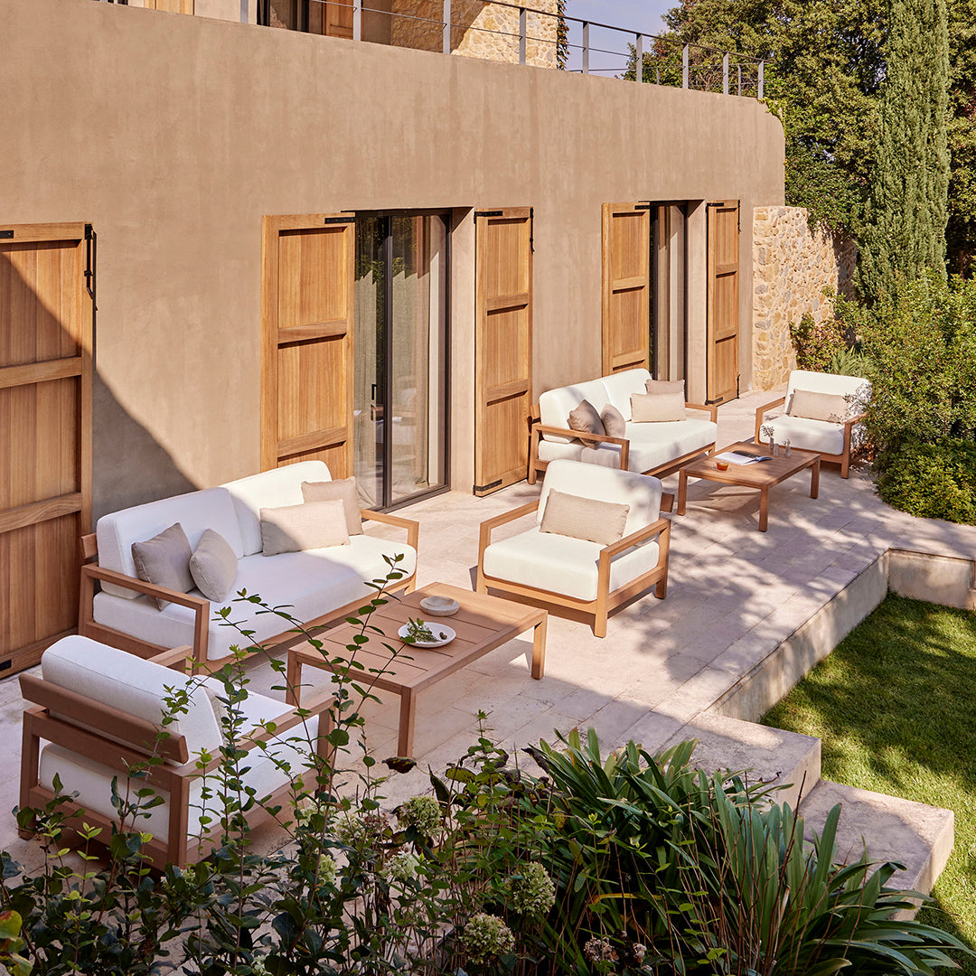 Modern outdoor seating set in neutral tones with cream cushions and natural wood accents against a serene green backdrop.