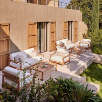 Modern outdoor seating set in neutral tones with cream cushions and natural wood accents against a serene green backdrop.