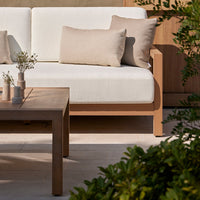 Light beige cushions on a white sofa, paired with a natural wood table and green foliage accents. Modern outdoor decor.