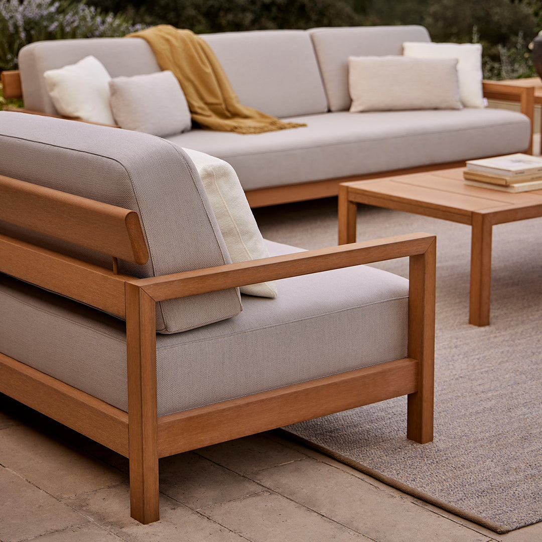 Light gray outdoor sofa with wooden frame, cream cushions, and a mustard throw draped over the armrest.