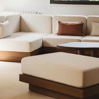 Beige sectional sofa with light wood accents and a decorative rust-colored pillow, featuring a minimalist design.