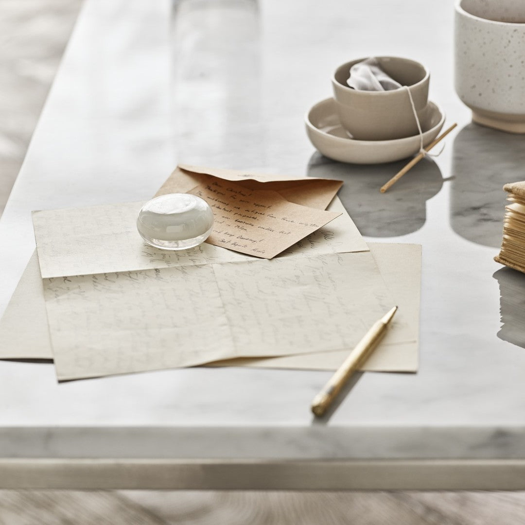 Neutral-toned stationery and ceramic bowls on a glossy marble table, featuring soft textures and subtle patterns.