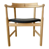 Natural wood chair with a light oak finish and a sleek black leather seat, featuring minimalistic design.
