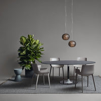 Modern dining setup with gray chairs, a round dark table, black and gold pendant lights, and a vibrant green plant.