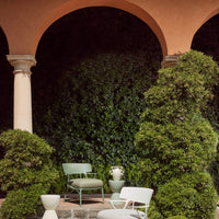 "Soft green and muted gray chairs against a lush green backdrop, with light stone and white accents in a serene outdoor setting."