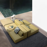 Yellow modular sofa with polka dot and floral patterned cushions, set against a sleek gray rug by a poolside.