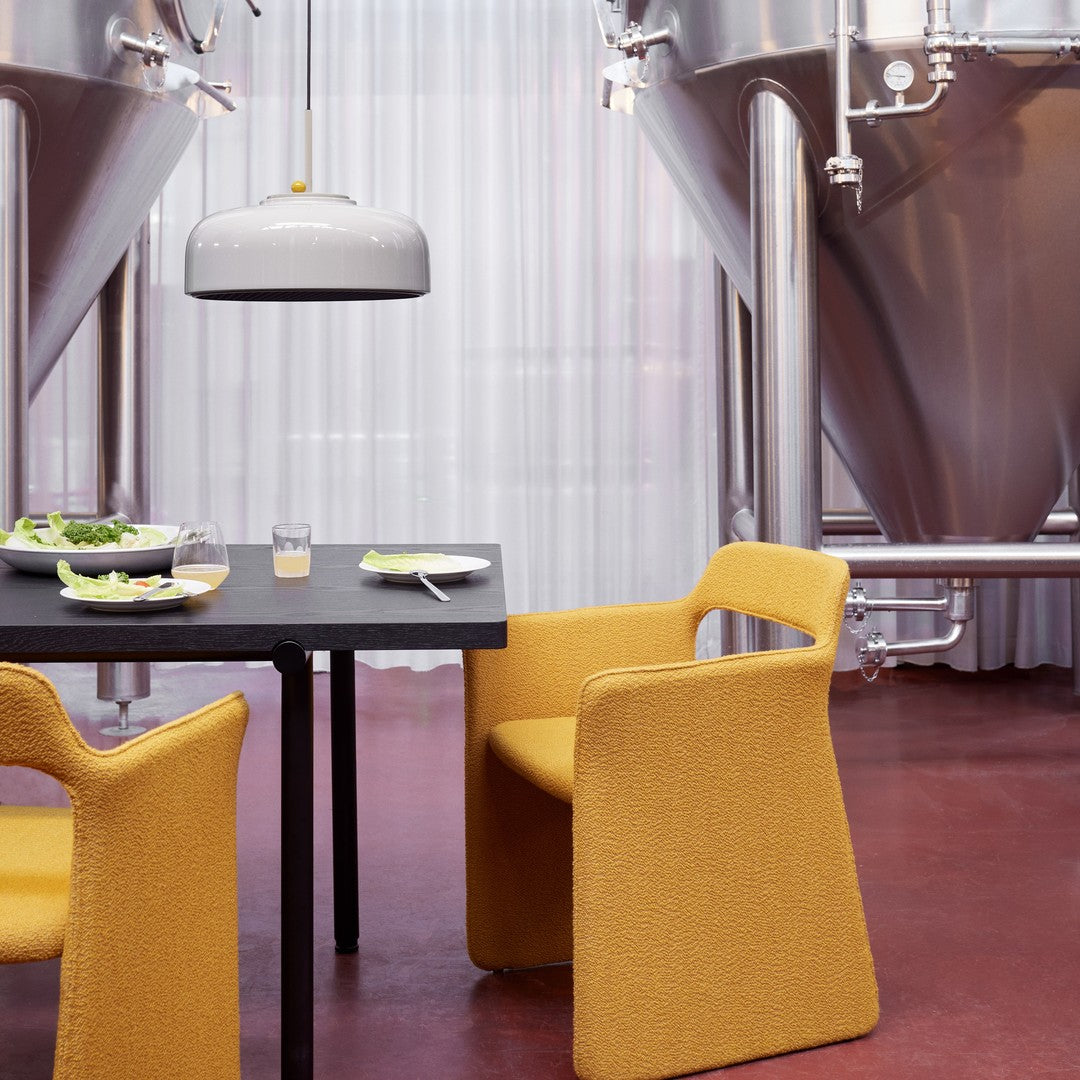 Yellow textured chairs and a sleek gray lamp contrast with a black table and stainless steel brewing tanks.