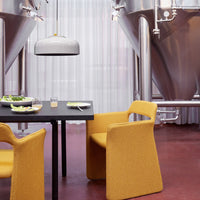 Yellow textured chairs and a sleek gray lamp contrast with a black table and stainless steel brewing tanks.