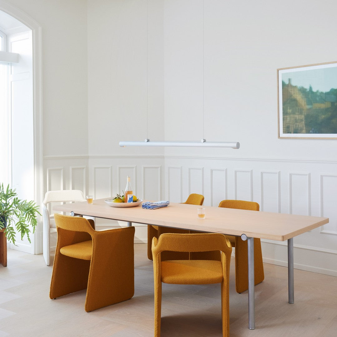 Bright yellow chairs around a light wooden table, complemented by a white pendant light and neutral walls.