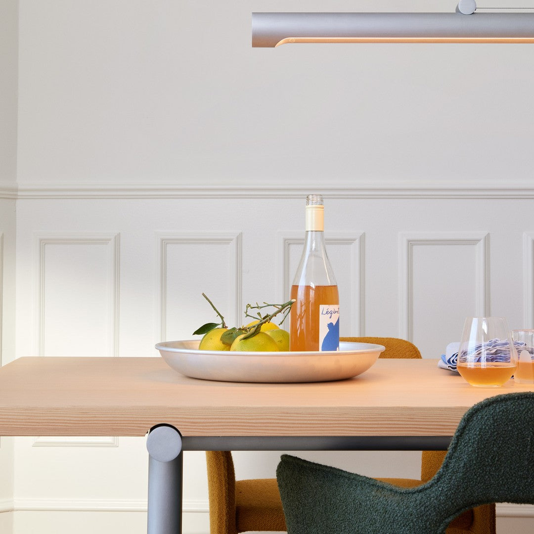 Stylish wooden table with matte beige surface, green and mustard chairs, silver accents, and a round white platter with oranges.