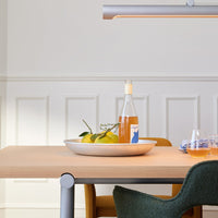 Stylish wooden table with matte beige surface, green and mustard chairs, silver accents, and a round white platter with oranges.