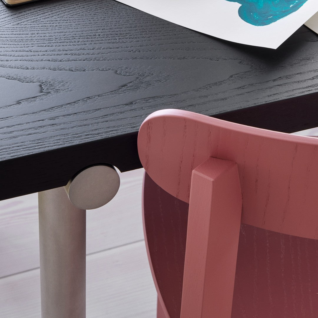 Modern black wood table with sleek silver accents and a soft pink chair, showcasing contemporary color contrasts and textures.