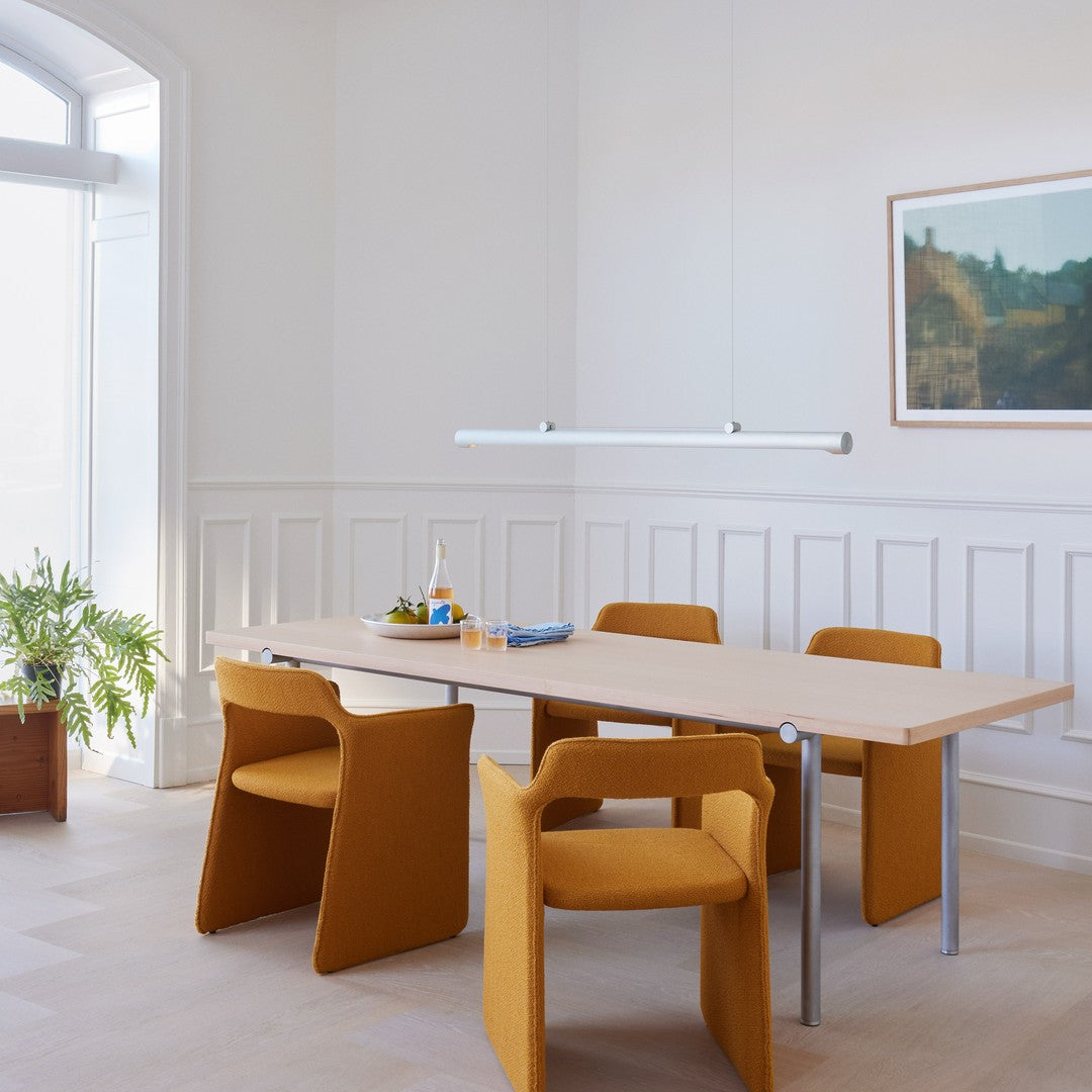 Modern dining room featuring wooden table and bold mustard yellow chairs against a bright, neutral backdrop.
