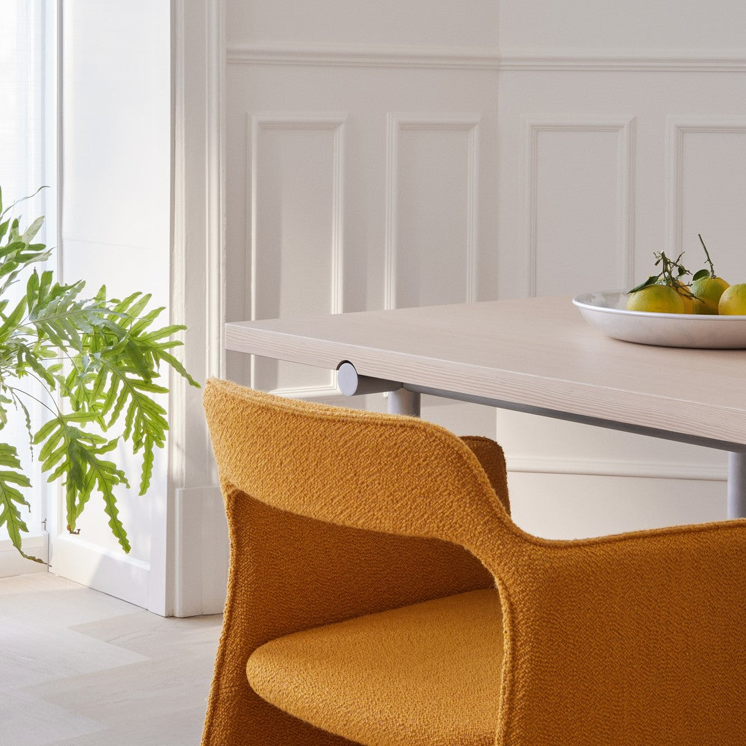 Stylish orange chair and light wood table against a neutral backdrop, accented by green leafy plant and white dish.