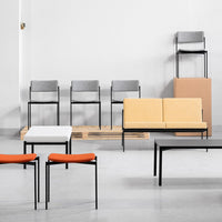Colorful modern seating: orange and yellow cushions, white and black tables, gray and black chairs against a neutral backdrop.