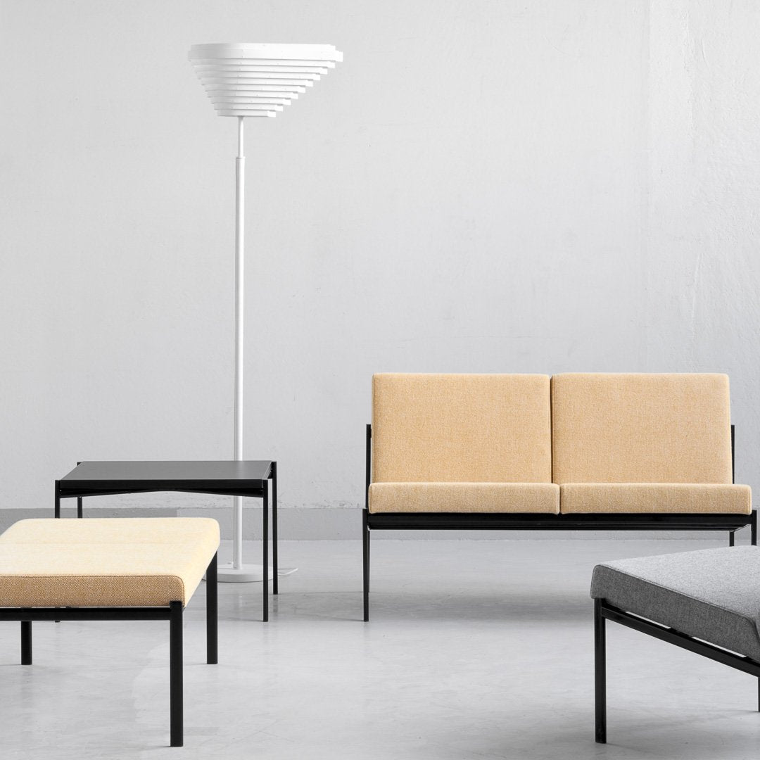 "Modern furniture set featuring beige cushions, black metal frames, and a sleek white lamp against a gray backdrop."