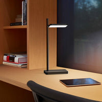 Black LED desk lamp on a natural wood surface, complemented by dark and light tones in the surrounding decor.