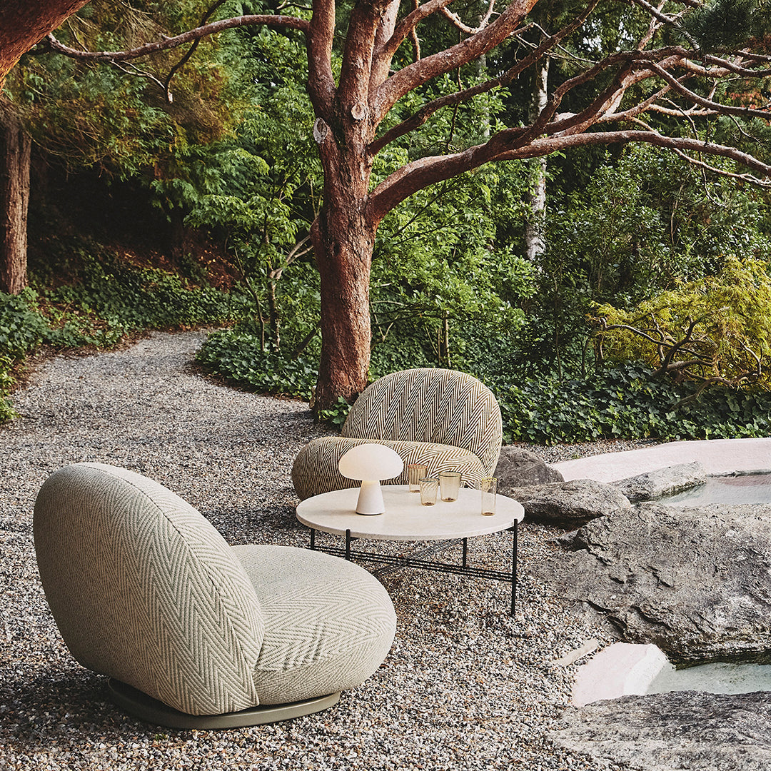 Soft beige lounge chairs with textured, organic patterns, set against a lush green outdoor backdrop.