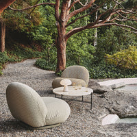 Soft beige lounge chairs with textured, organic patterns, set against a lush green outdoor backdrop.