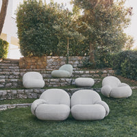 Light gray and soft green plump outdoor lounge chairs set against a stone wall and lush greenery.