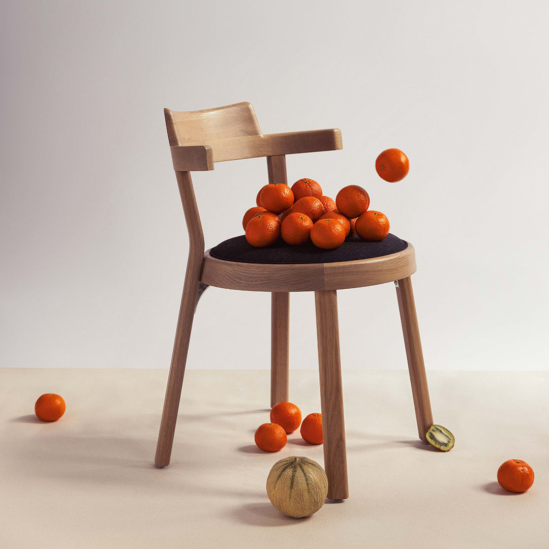 Stylish wooden chair with a black seat, surrounded by vibrant orange citrus fruits. Minimalistic design and soft colors.