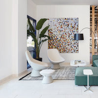 Modern lounge area featuring white chairs, green sofa, textured gray rug, and colorful abstract wall art.