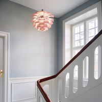 Modern pendant light in soft pink with layered design, set against a pale blue wall and white staircase railing.