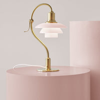 Pink lamp with layered white shades and a sleek gold base set against soft pink cylinders.