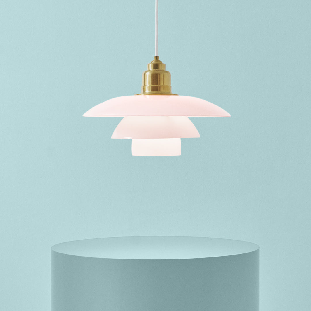 Pink layered pendant lamp with a brass finish against a soft blue background. Modern design with elegant curves.