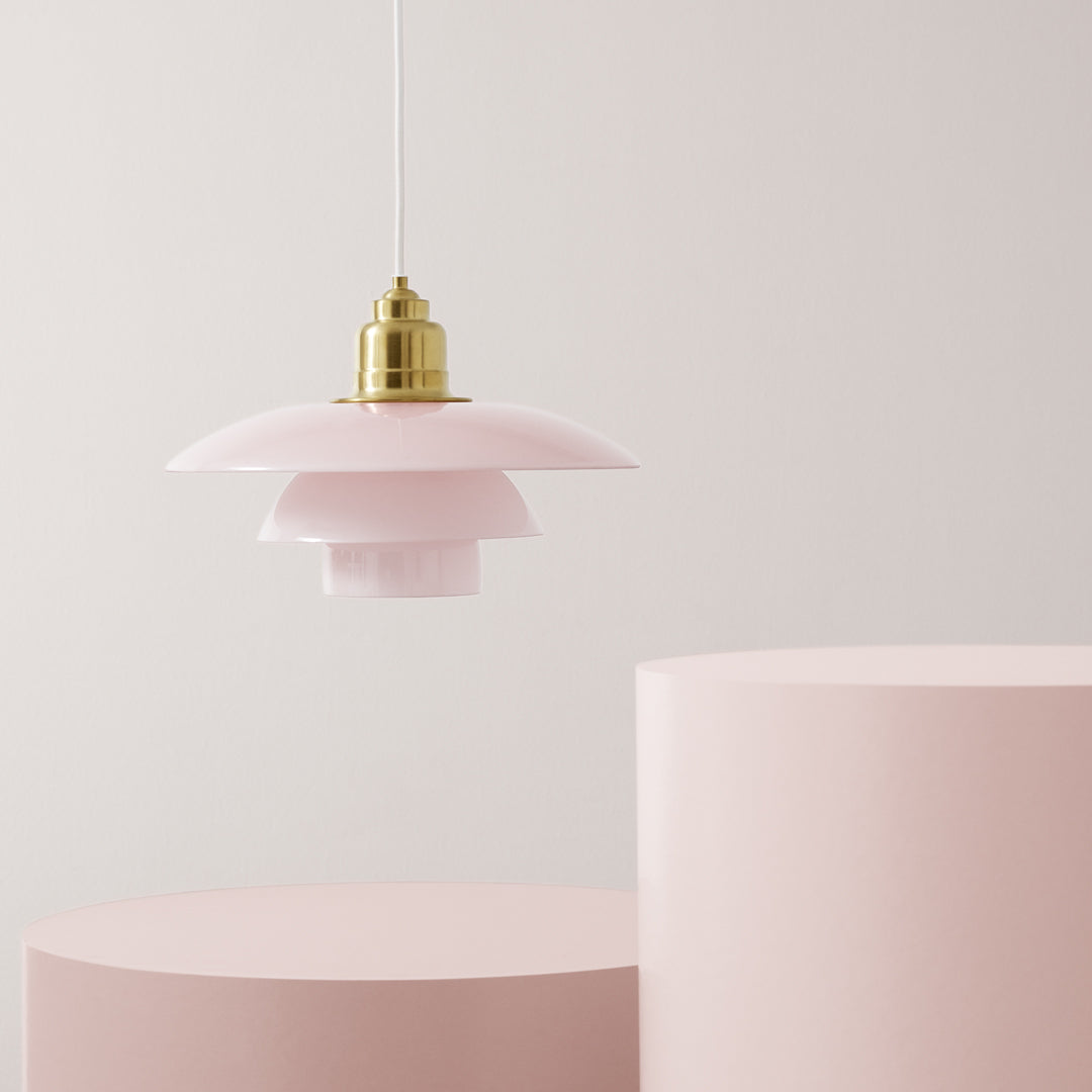 Pink pendant lamp with layered shades and gold accents, against soft pink cylindrical bases. Elegant and modern design.