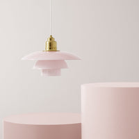 Pink pendant lamp with layered shades and gold accents, against soft pink cylindrical bases. Elegant and modern design.