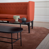 "Modern living room with an orange couch, black coffee table, green ceramic bowl, and brown rug."