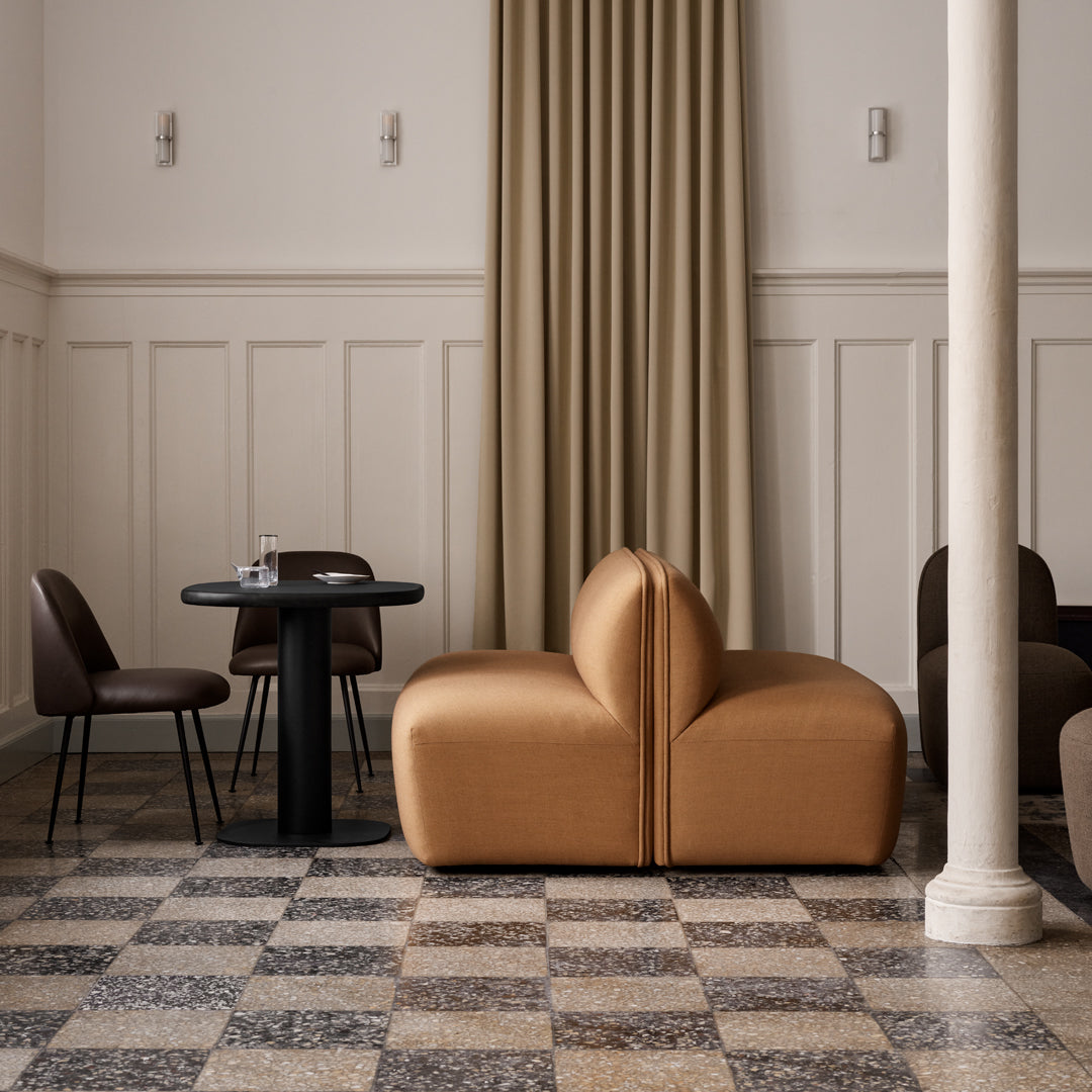 Stylish brown sofa with smooth, curved lines, paired with dark chairs on a patterned black-and-white checkered floor.
