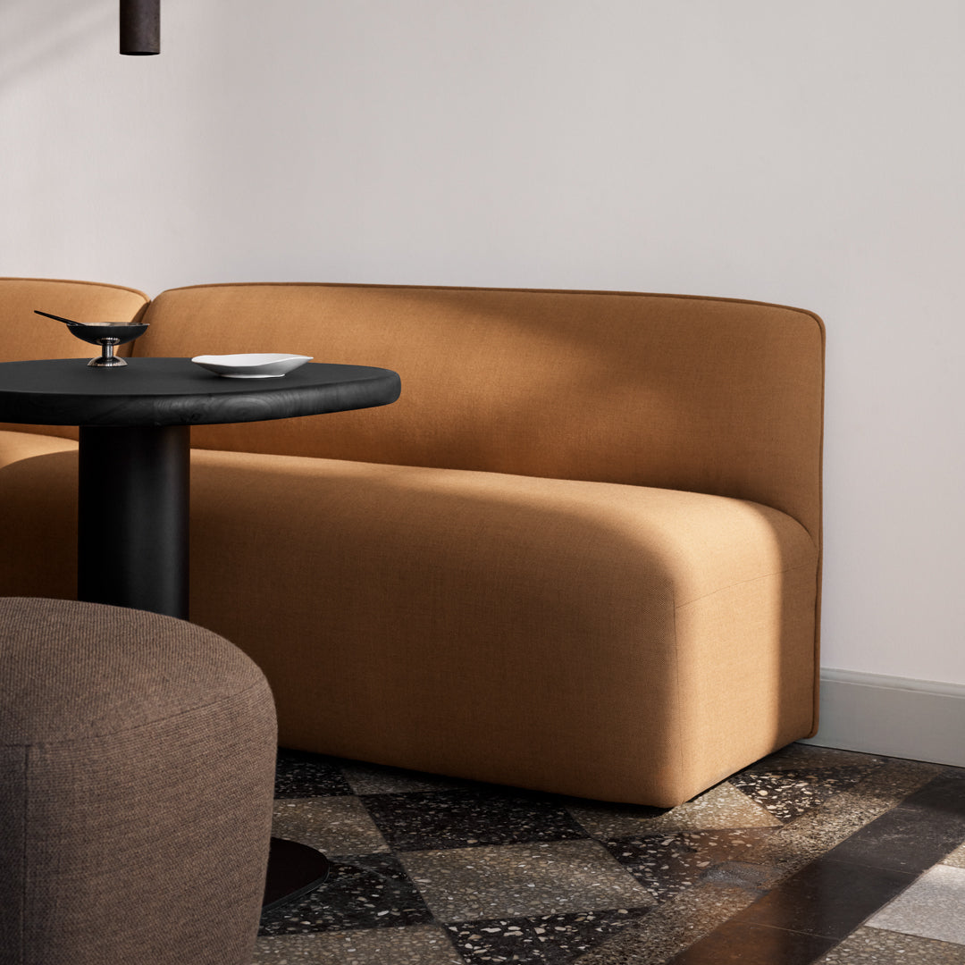 Rusty brown curved sofa with a smooth texture, paired with a black round table and patterned floor tiles.