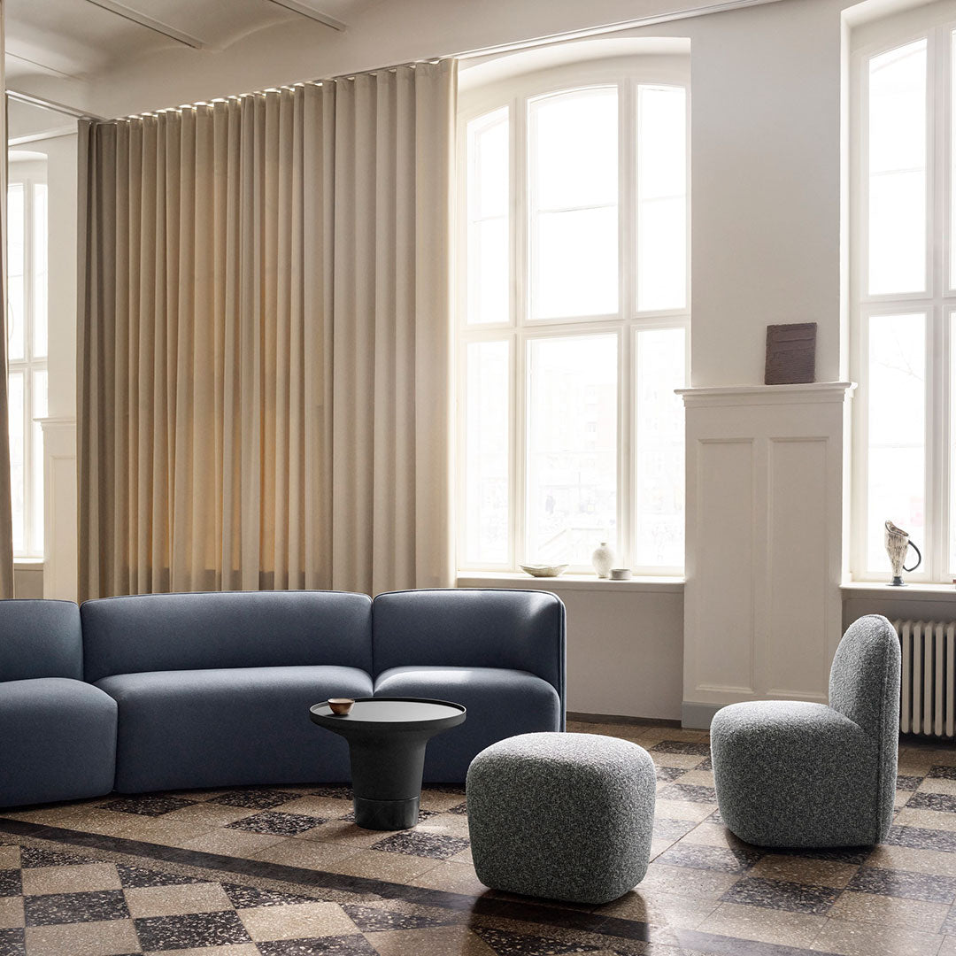 Modern living room featuring a blue curved sofa, round black table, and textured gray accent chairs against beige curtains.