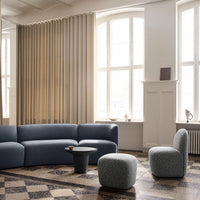 Modern living room featuring a blue curved sofa, round black table, and textured gray accent chairs against beige curtains.
