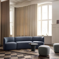 Modern blue curved sofa with soft fabric, paired with neutral-toned curtains and geometric patterned floor tiles.