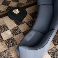 Elegant blue sofa on a patterned black and white tiled floor, featuring a round black side table.