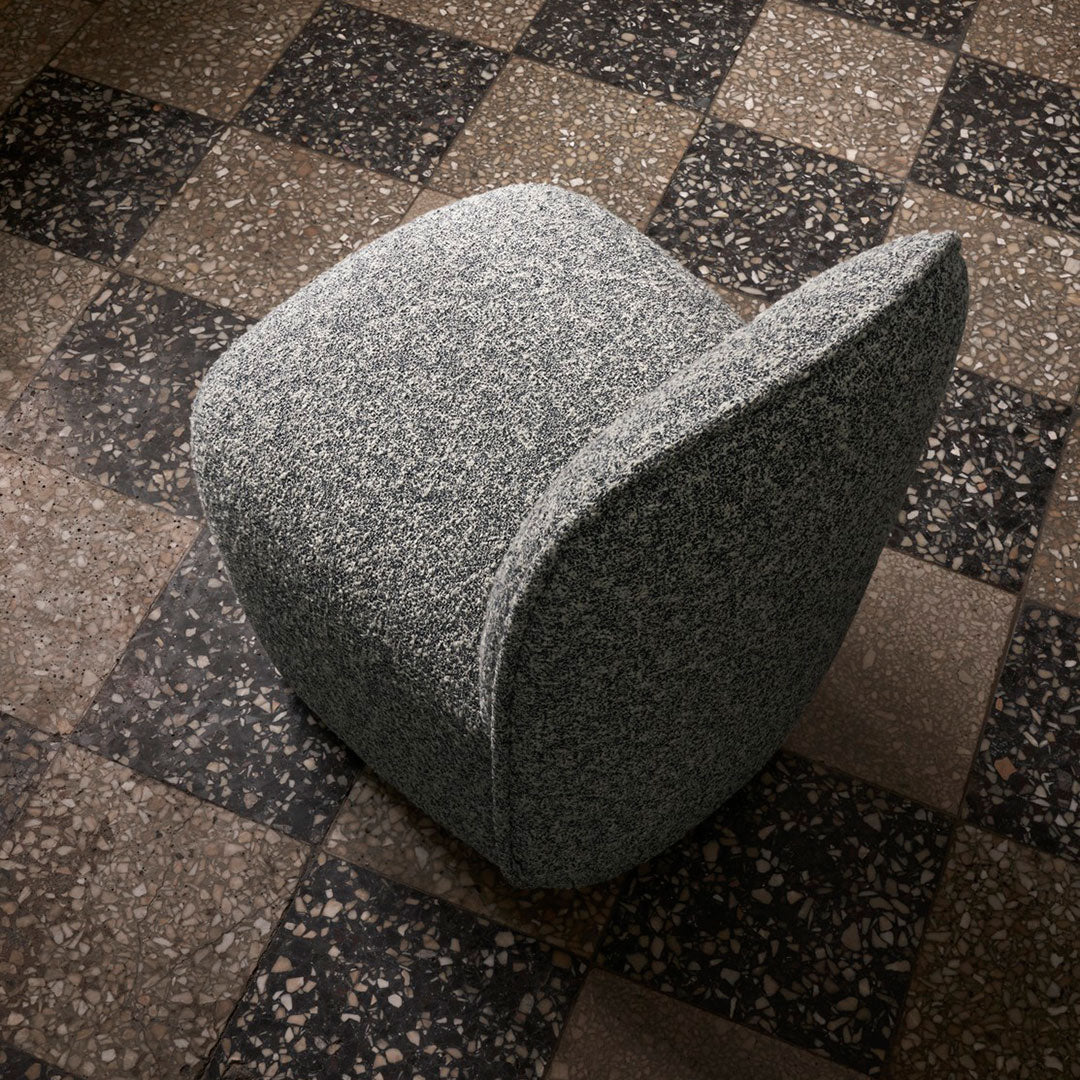 Gray textured chair on a checkered brown and black floor. Modern design with soft curves and subtle patterns.